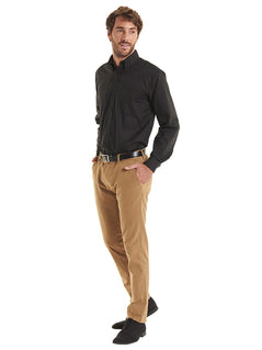 Person wearing Uneek Clothing UC701 Mens Pinpoint Oxford Full Sleeve Shirt long sleeve in black with collar and front with black buttons, pocket on left chest .